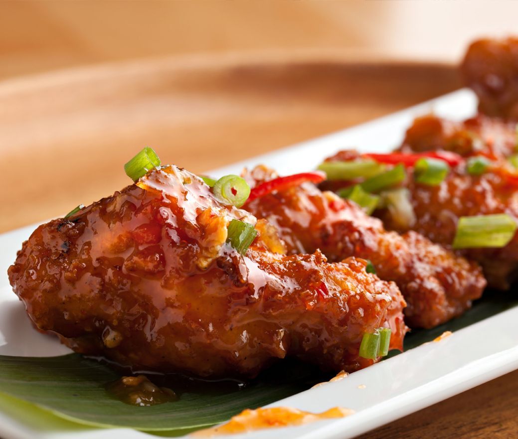 Glazed chicken wings topped with chopped green onions on a white plate