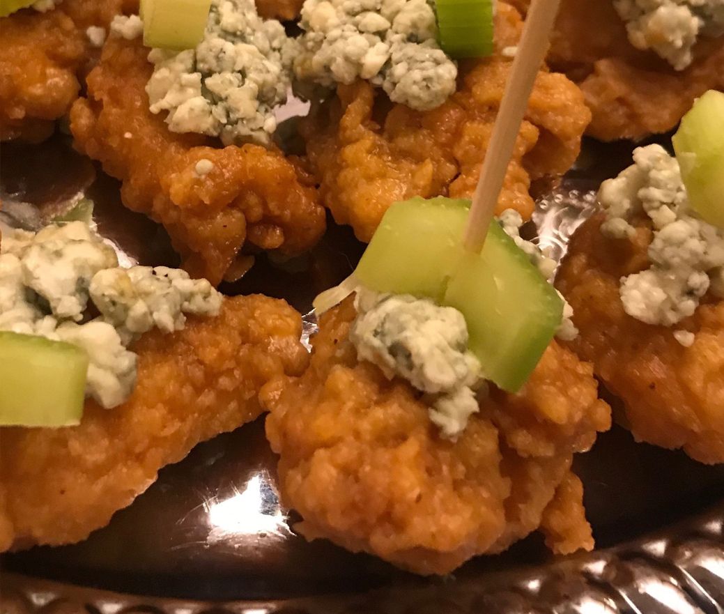 Fried chicken bites topped with blue cheese crumbles and celery on a serving tray