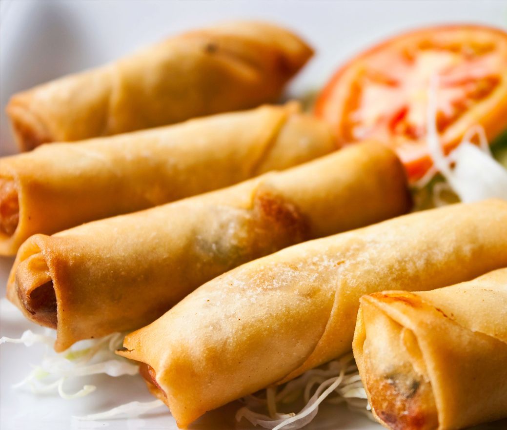 Golden fried spring rolls on a plate with shredded cabbage and tomato slices