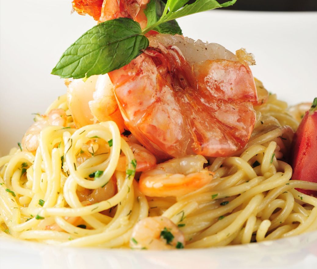 Plated spaghetti with shrimp and basil garnish on a white background