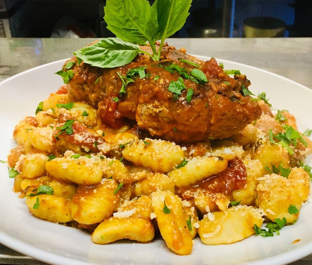 Plate of gnocchi topped with a large sauced meat cutlet, garnished with herbs and grated cheese.