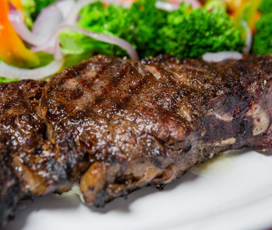 Grilled steak on a white plate with green garnish and onion slices