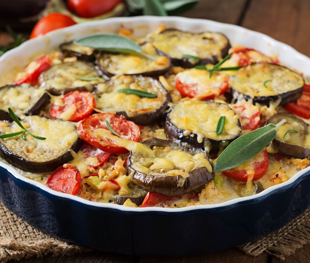 Baked vegetable gratin with eggplant, tomatoes, and basil in a round ceramic dish
