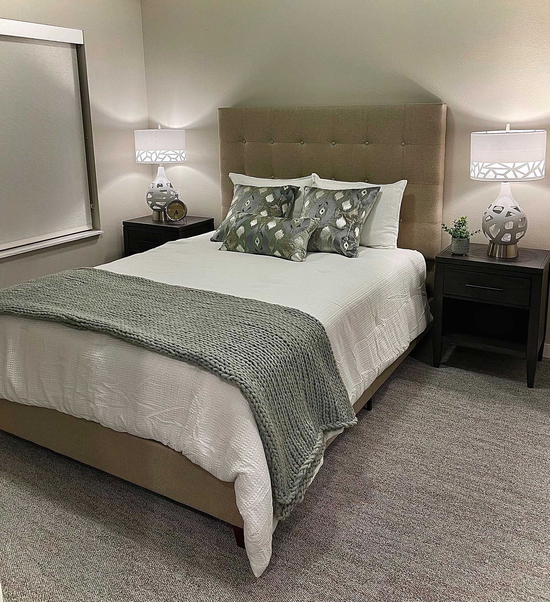 A bedroom with a bed , nightstand , lamps and a rug.