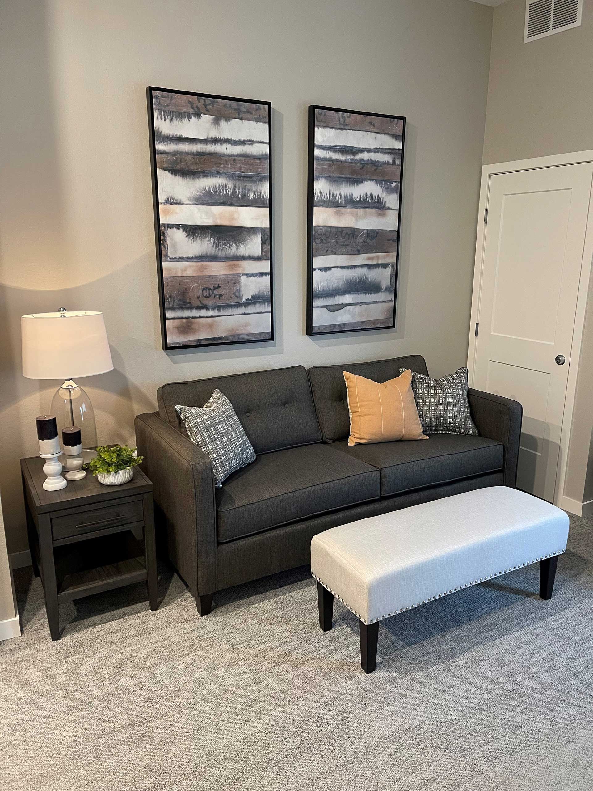A living room with a couch , ottoman , table and two paintings on the wall.