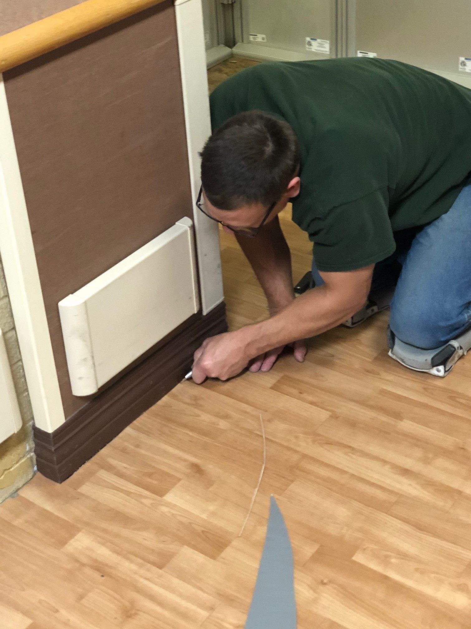 A man in a green shirt is kneeling down on a wooden floor