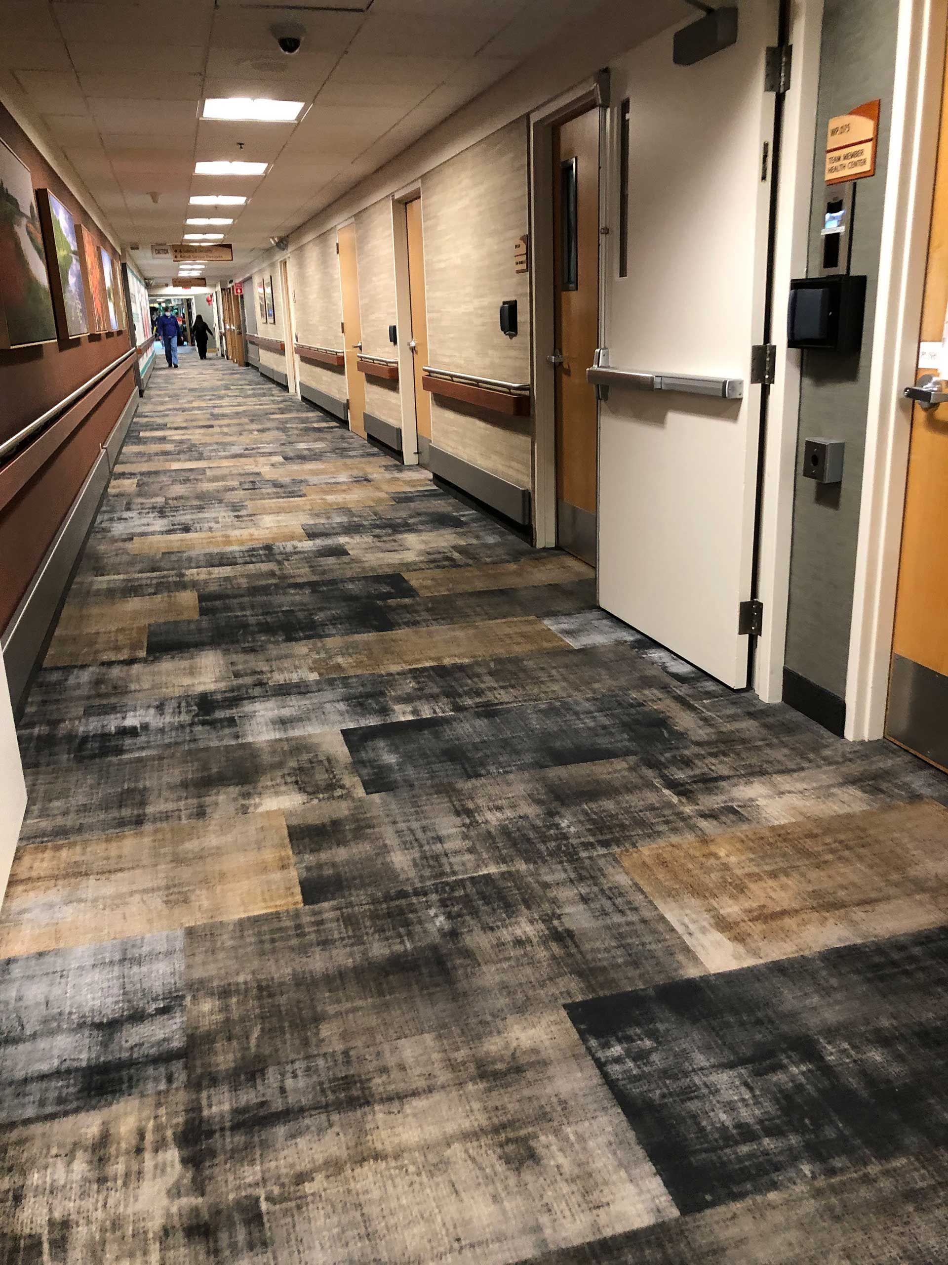 A long hallway with a carpeted floor and doors in a hospital.