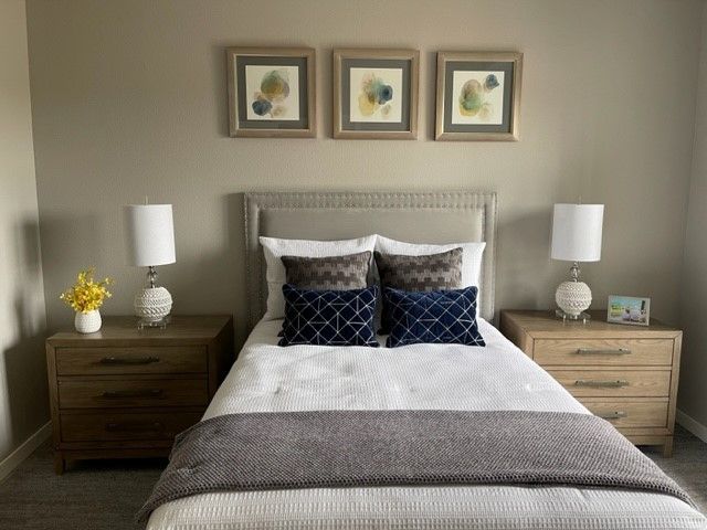 A bedroom with a bed , nightstands , lamps and three paintings on the wall.
