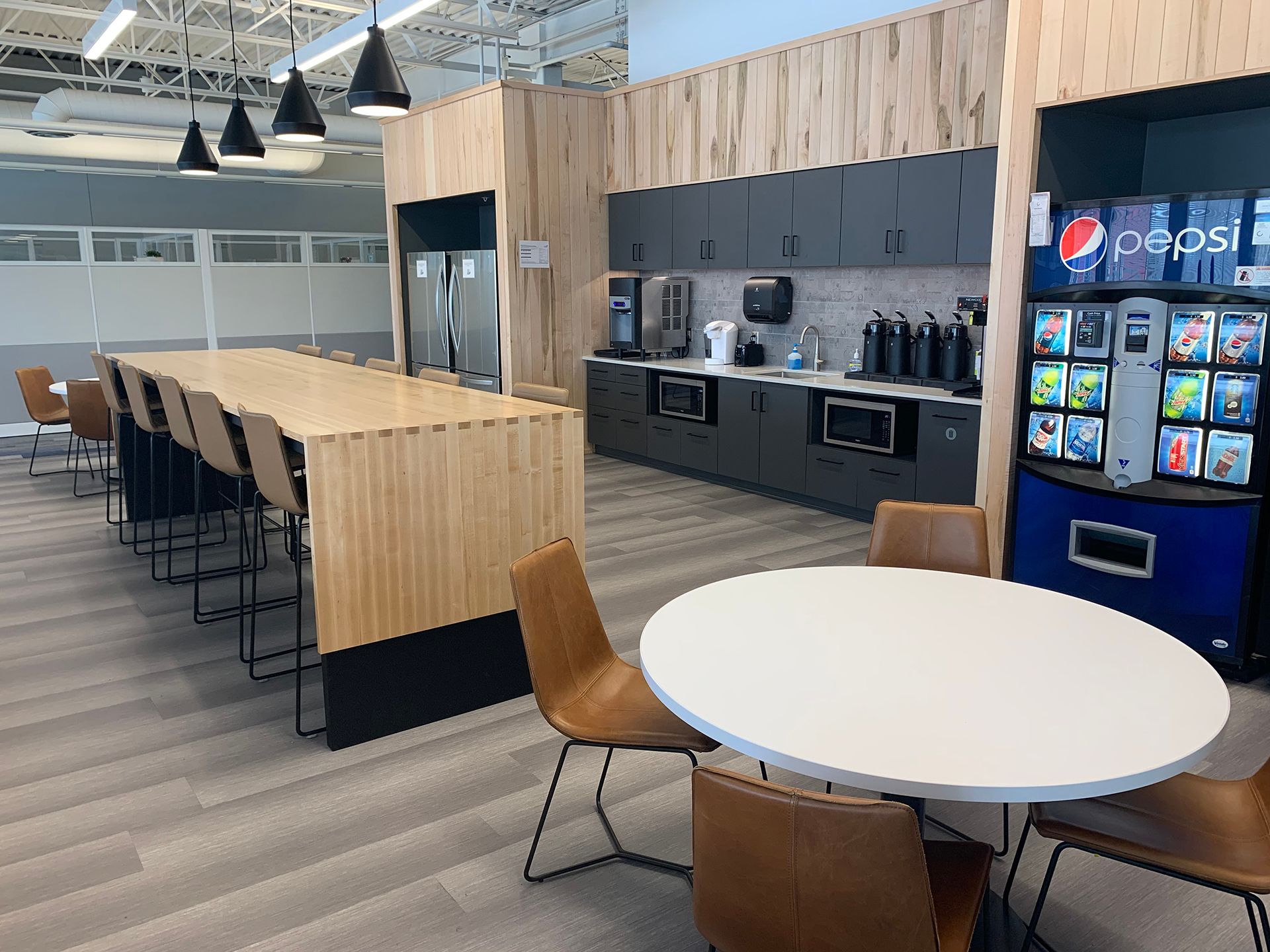 A kitchen with tables and chairs and a pepsi machine.