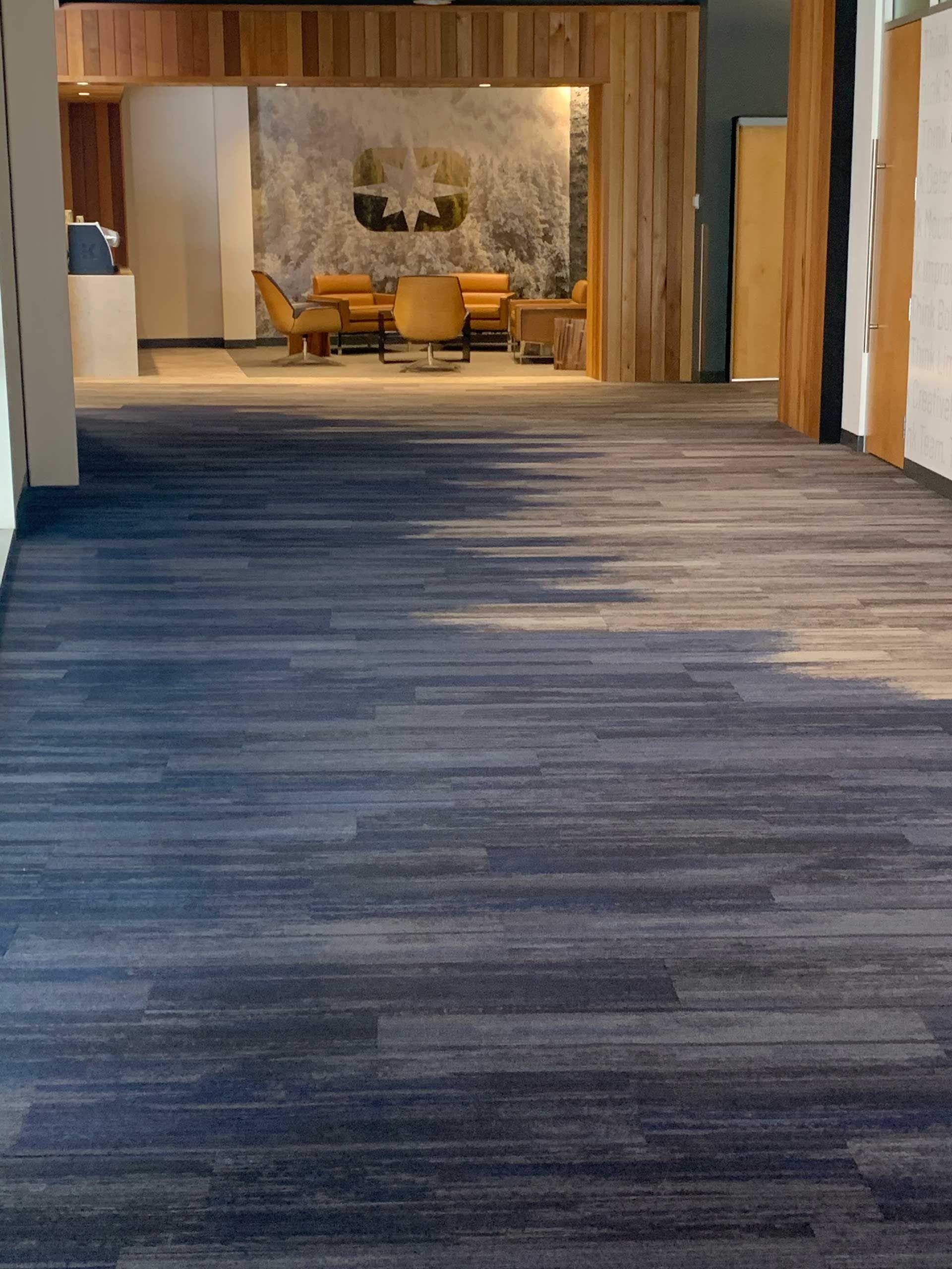 A long hallway with a blue carpet and a wooden wall.