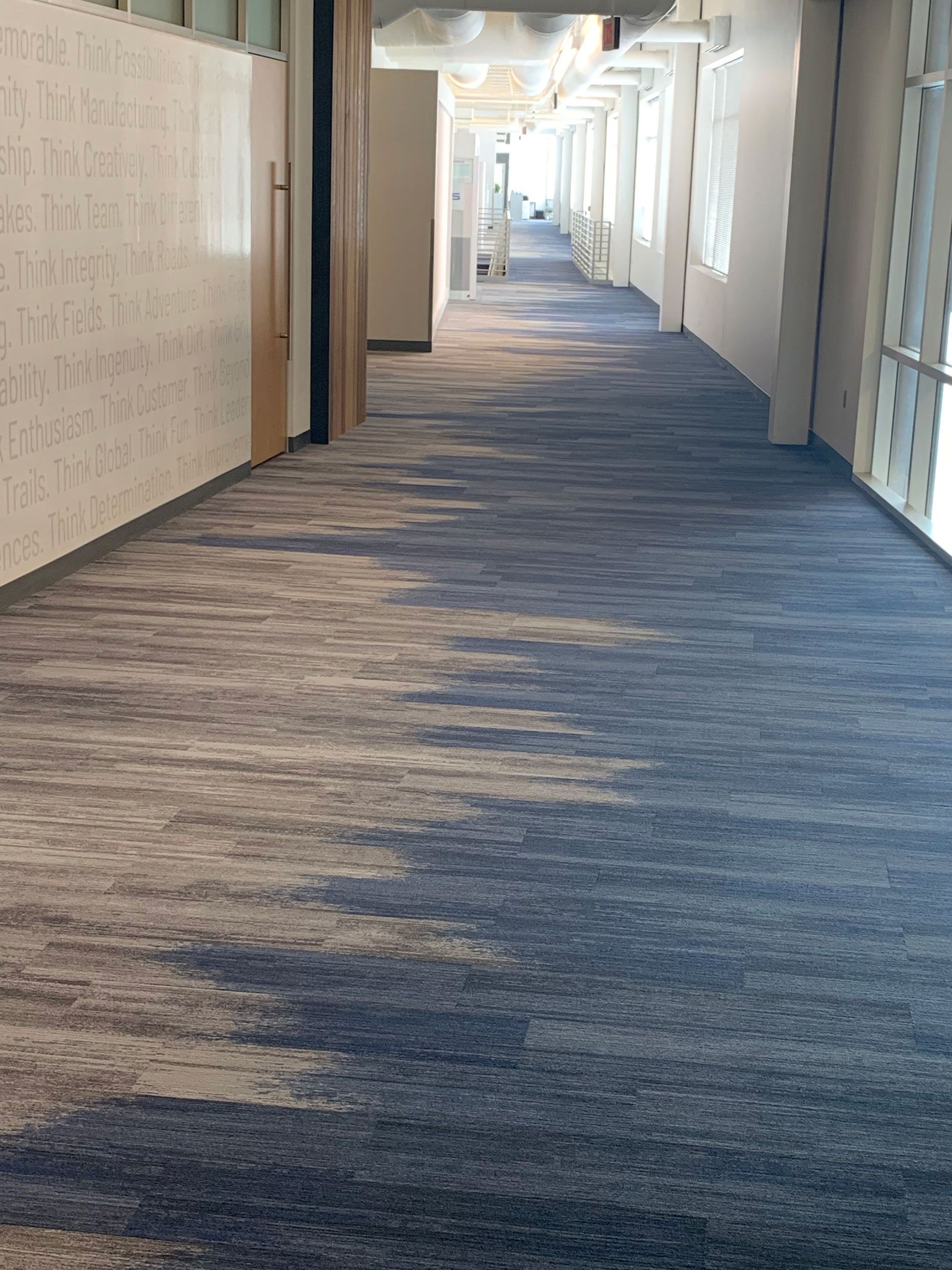 A long hallway with a blue carpet and a white wall.