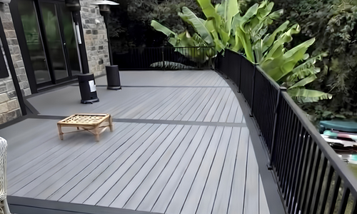 Modern gray deck with black railing, potted plant, and a low wooden table beside glass doors.