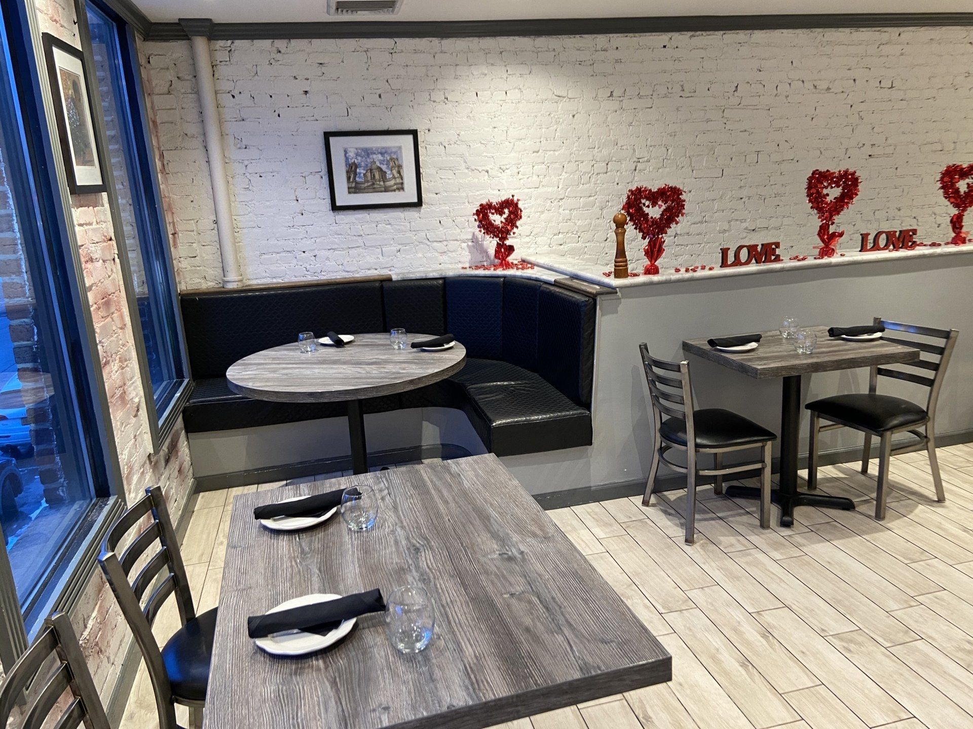 Restaurant interior with tables, a booth, and Valentine's Day decorations on a brick wall.