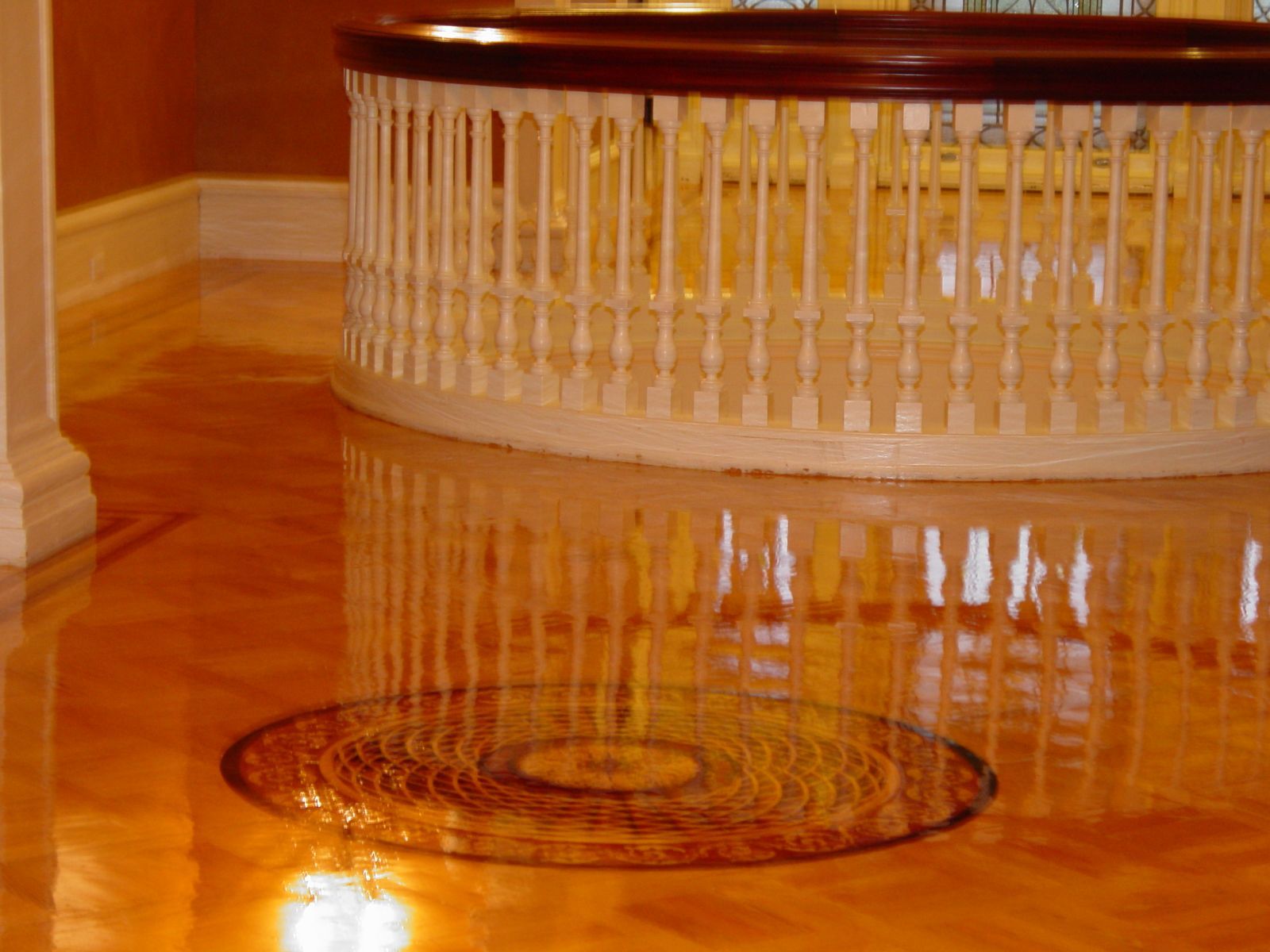 A wooden staircase with a white railing and a reflection of the railing in the floor.