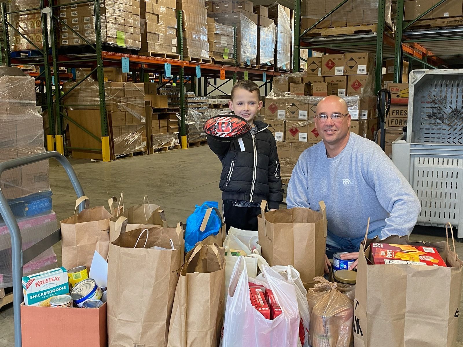 A man and a child are standing in a warehouse filled with bags of food.