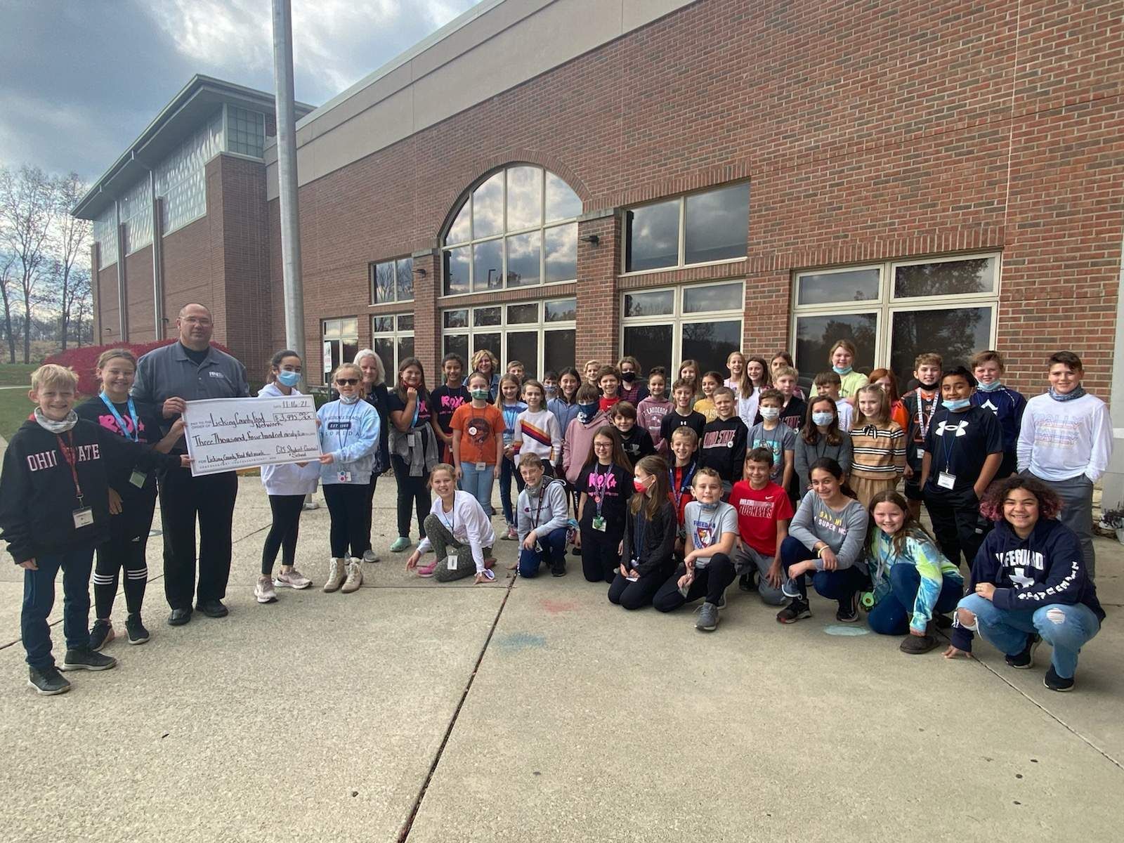 A group of children are standing in front of a brick building holding a check.