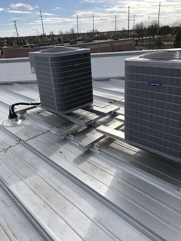 Two air conditioners are sitting on top of a metal roof