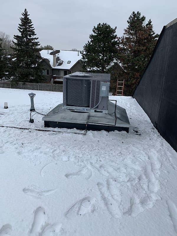 An air conditioner is sitting on top of a snow covered roof