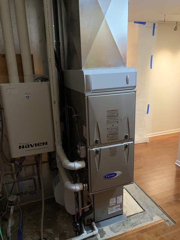 A stainless steel furnace is sitting in a basement next to a wooden floor