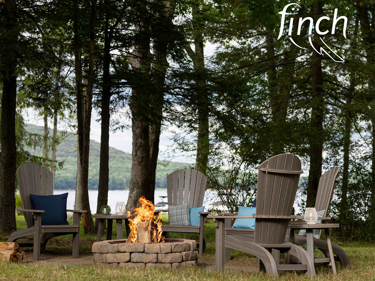 A fire pit is surrounded by chairs and a lake in the background