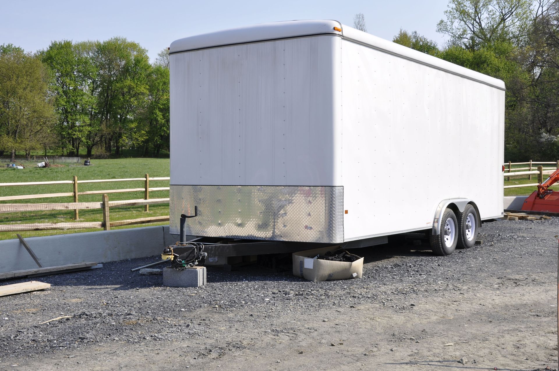 White cargo trailer on gravel, near a wooden fence and green field.