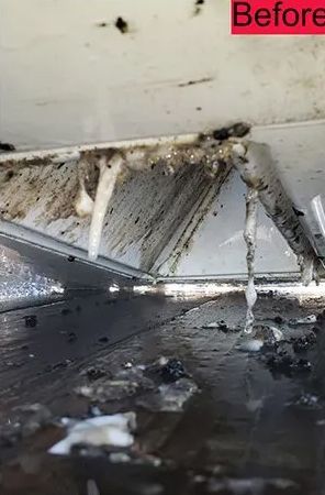 Close-up of dirty, dripping, white vent with streaks of grime and debris falling onto a wet surface.