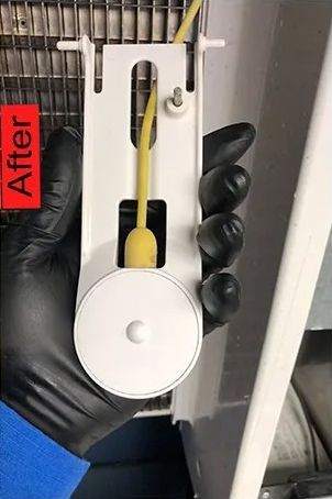 Black-gloved hand holding a white refrigerator component with yellow wiring. 