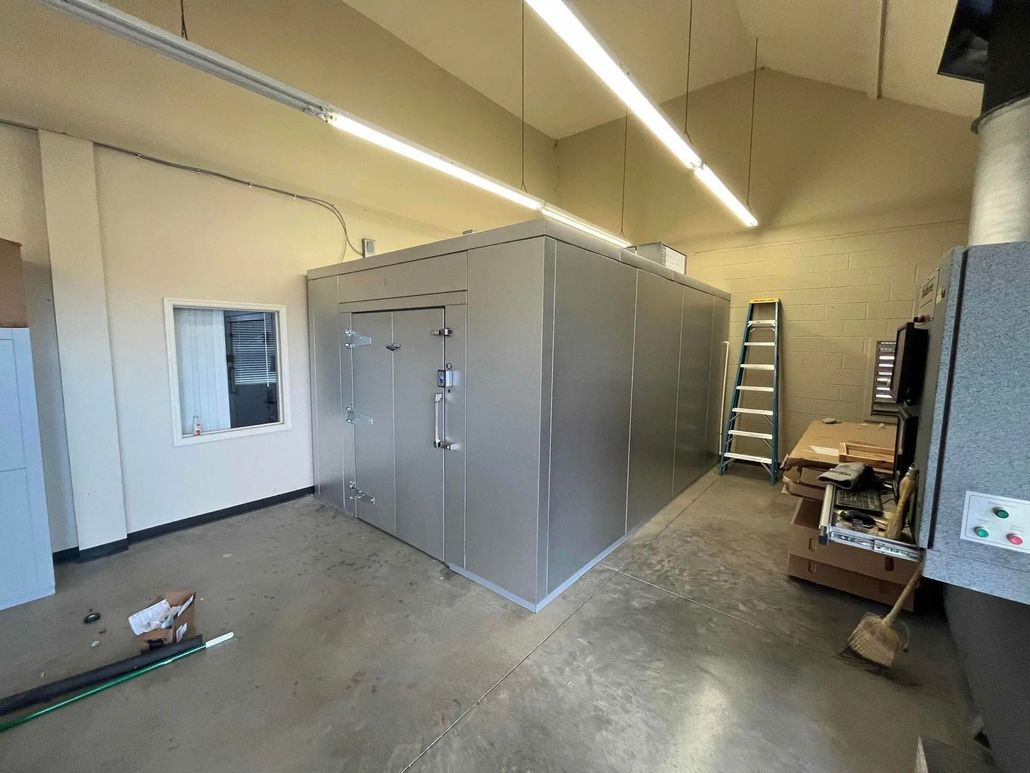 Large, metallic industrial enclosure in a room. A window, ladder, and equipment are nearby.