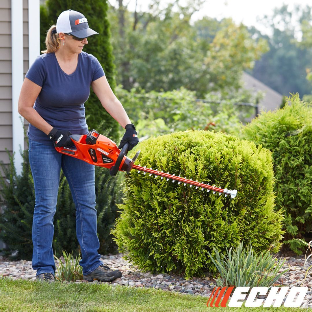 Woman trimming a bush with an orange hedge trimmer in a yard.