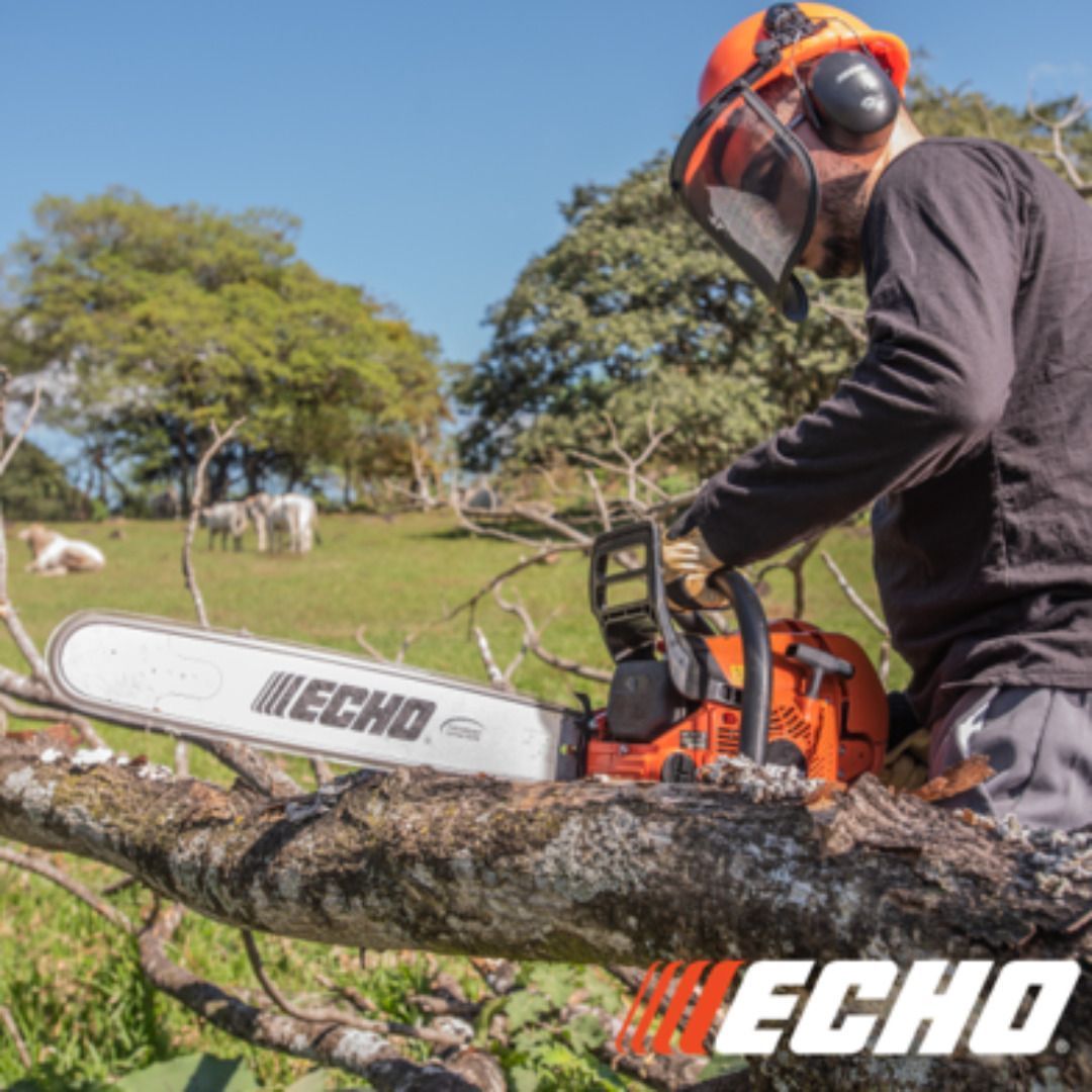 Man using an orange Echo chainsaw, cutting a tree branch in a sunny field. Protective gear visible.