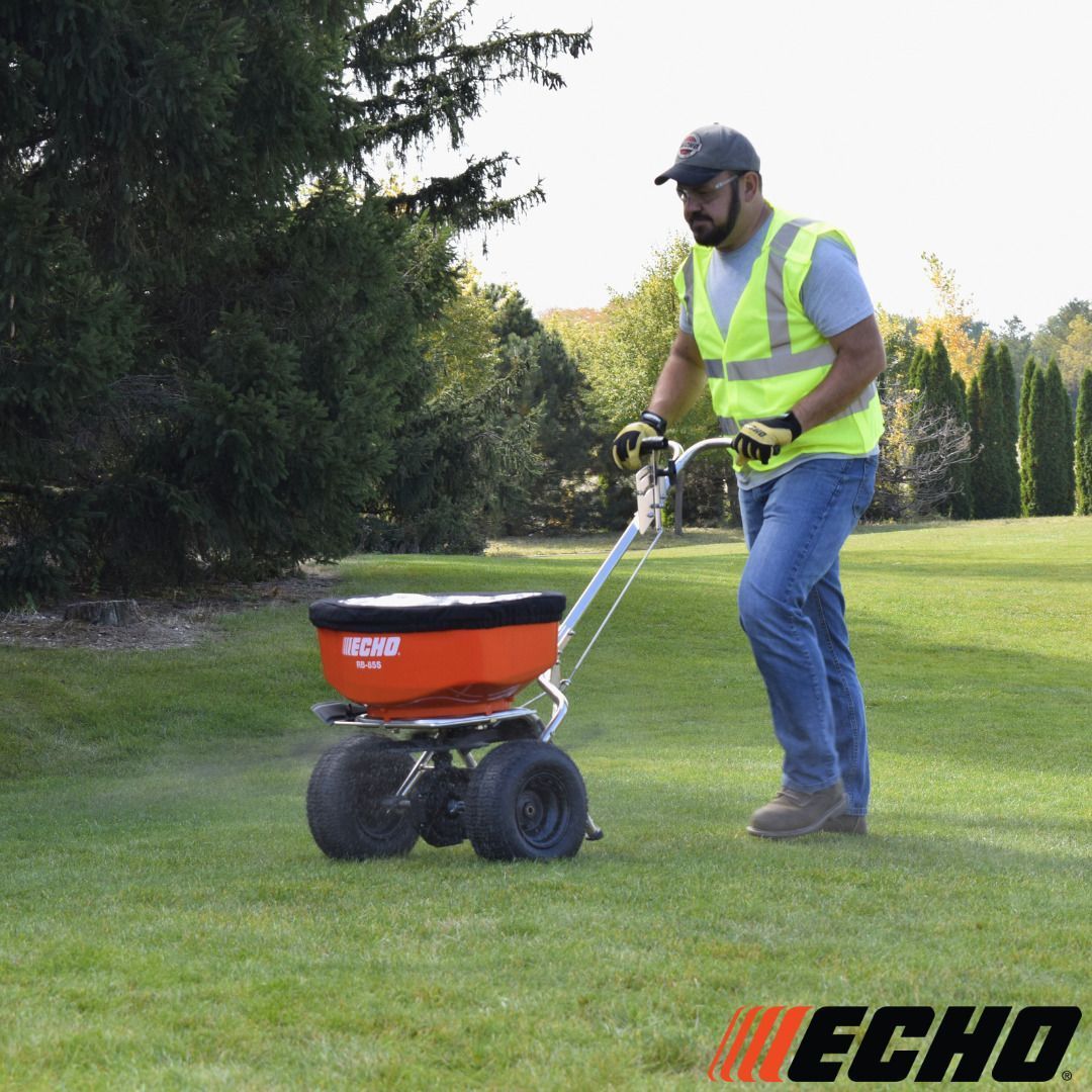 Man pushing an ECHO spreader on a lawn, applying material.