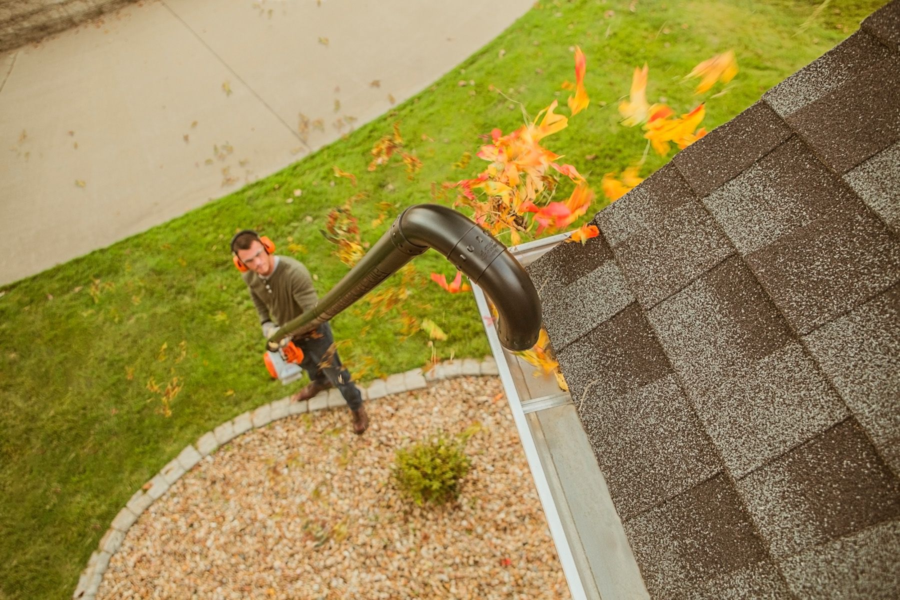 Man using a leaf blower to clear leaves from a gutter on a roof.