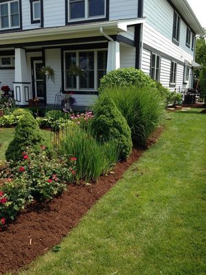 A house with white siding and a black trim, next to a landscaped garden with red mulch.