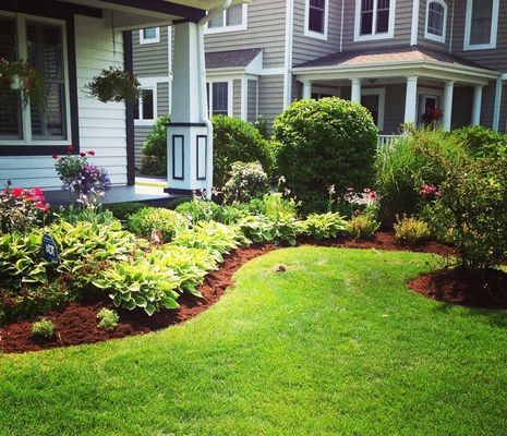 Well-manicured front yard with green grass, flower beds, and a house in the background.