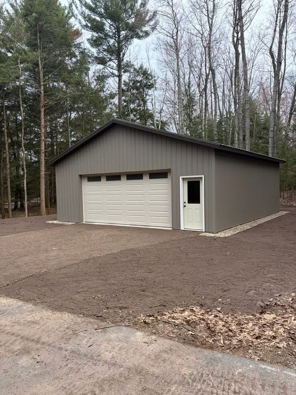 Gray garage with white door and side entry in a wooded yard