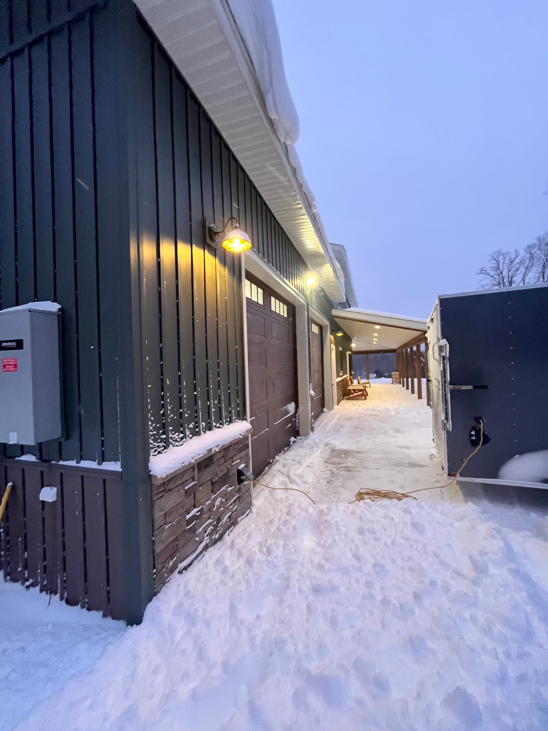 Exterior view of a building covered in snow, lit by overhead lights. Snowy ground and overcast sky.