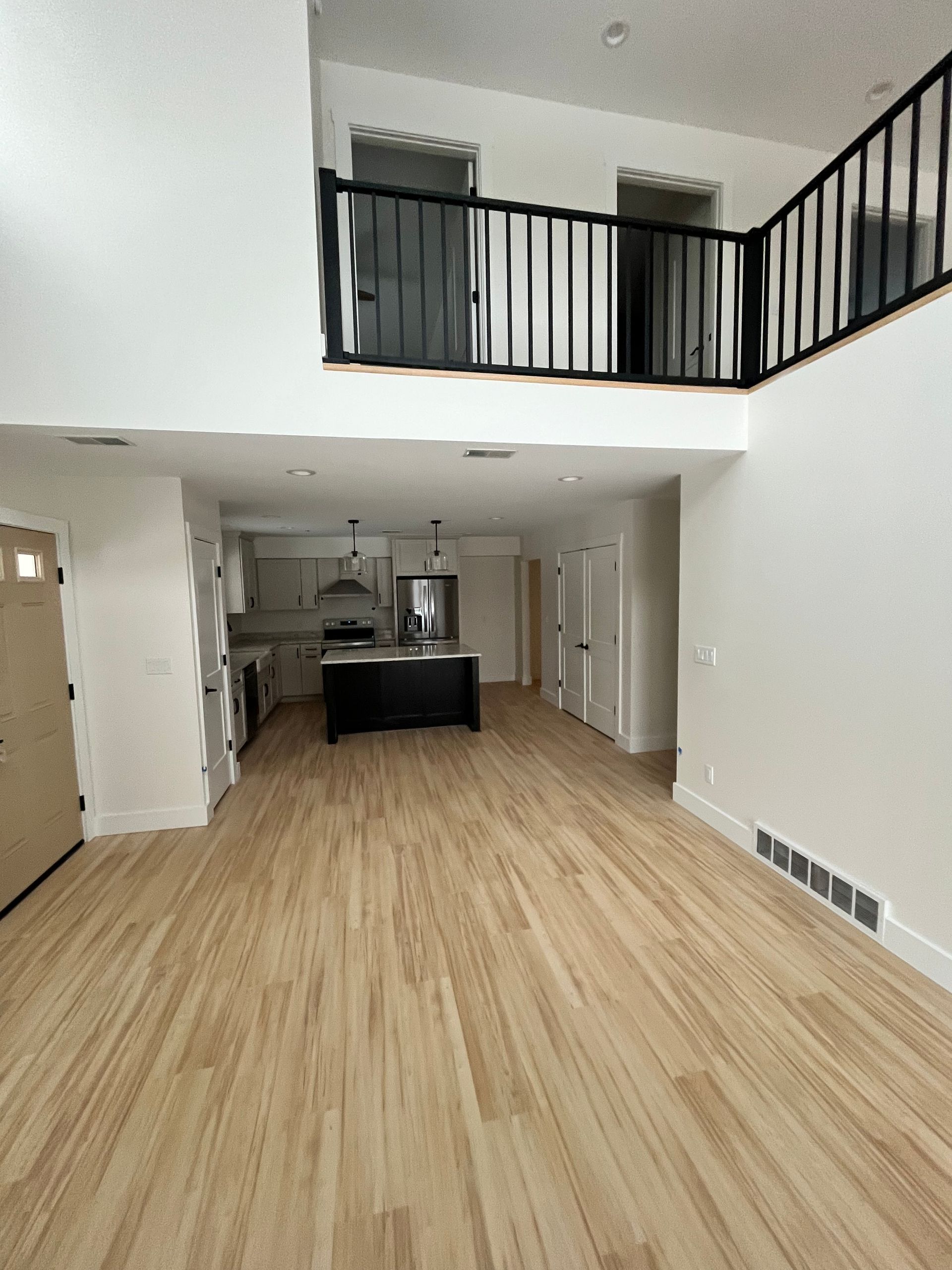 Spacious interior with hardwood floors, kitchen, and balcony with black railing.