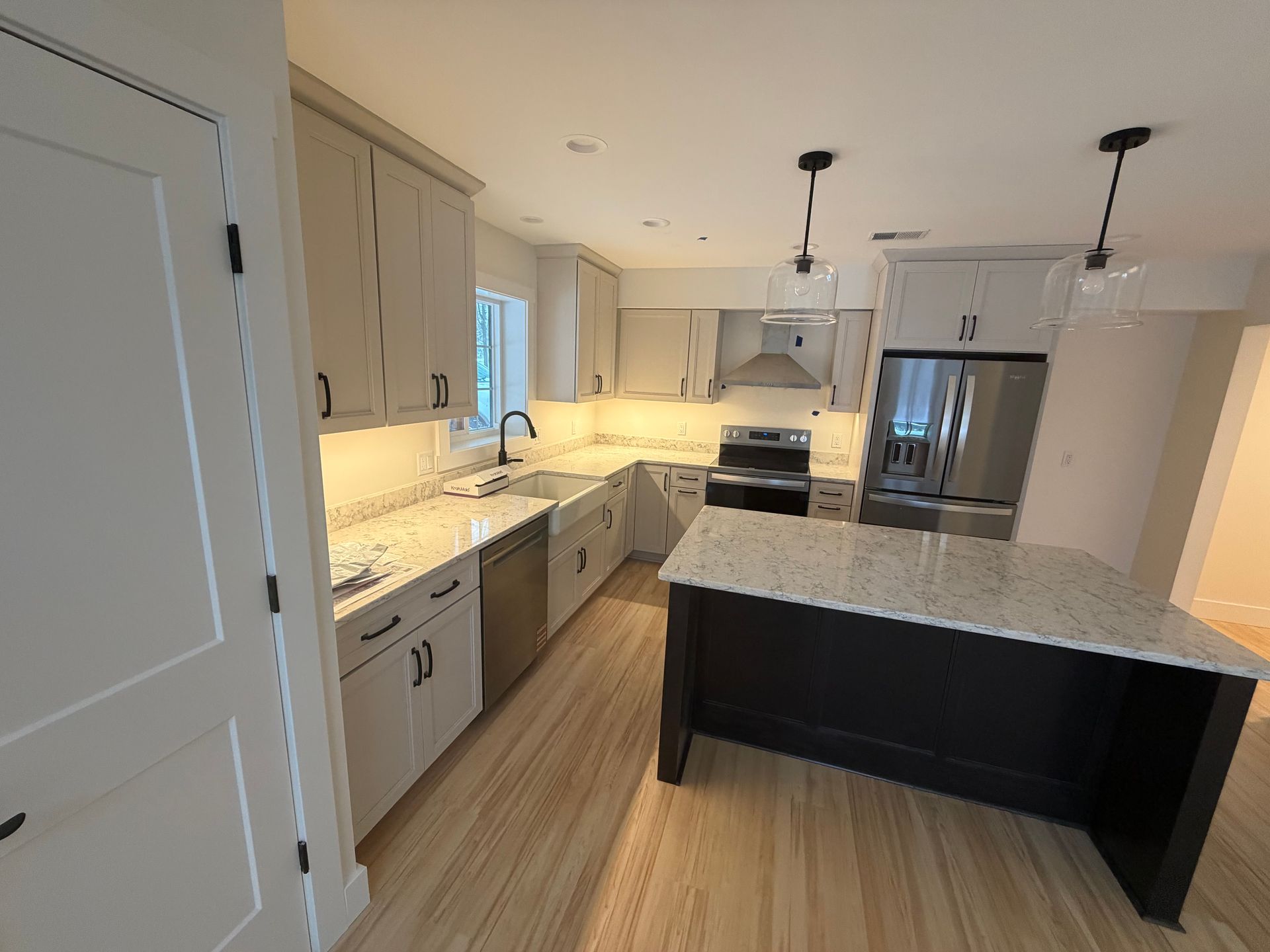 Modern kitchen with light gray cabinets, black island, stainless steel appliances, and wood floor.
