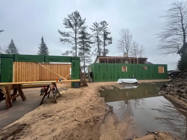 Construction site with green shipping containers, sandy ground, and a muddy puddle under overcast skies