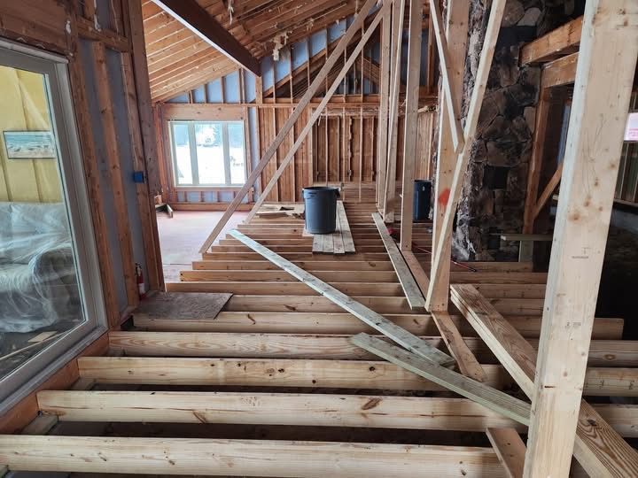 Interior of a house under construction with exposed wooden framing and unfinished floor joists.