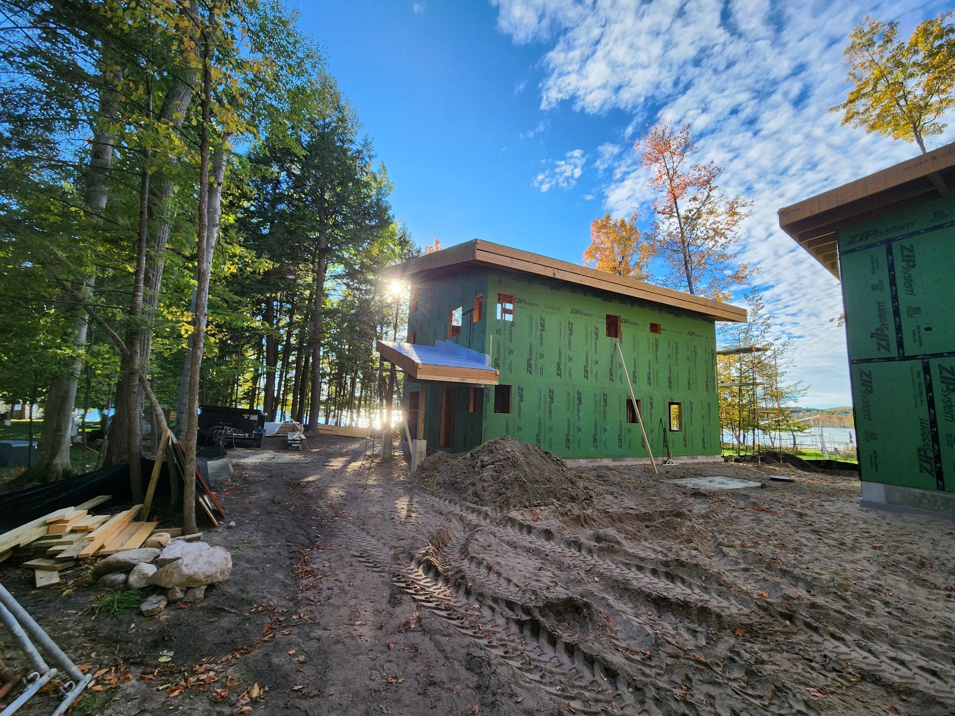 Construction site: Two-story house framed, green siding, partially built, sunny day, lake in background.