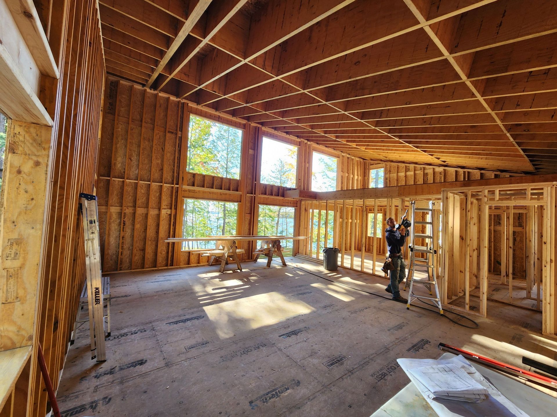 Interior of a house under construction. Wooden framework, windows, and a person working are visible.