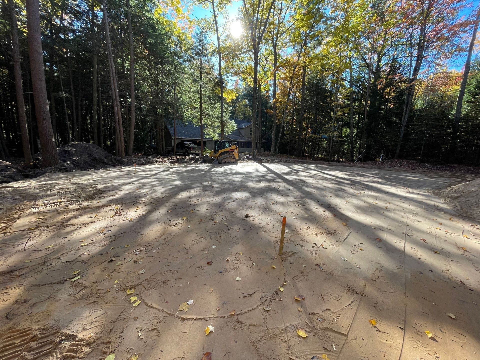 Dirt lot with excavator and surrounding trees; sunny day.