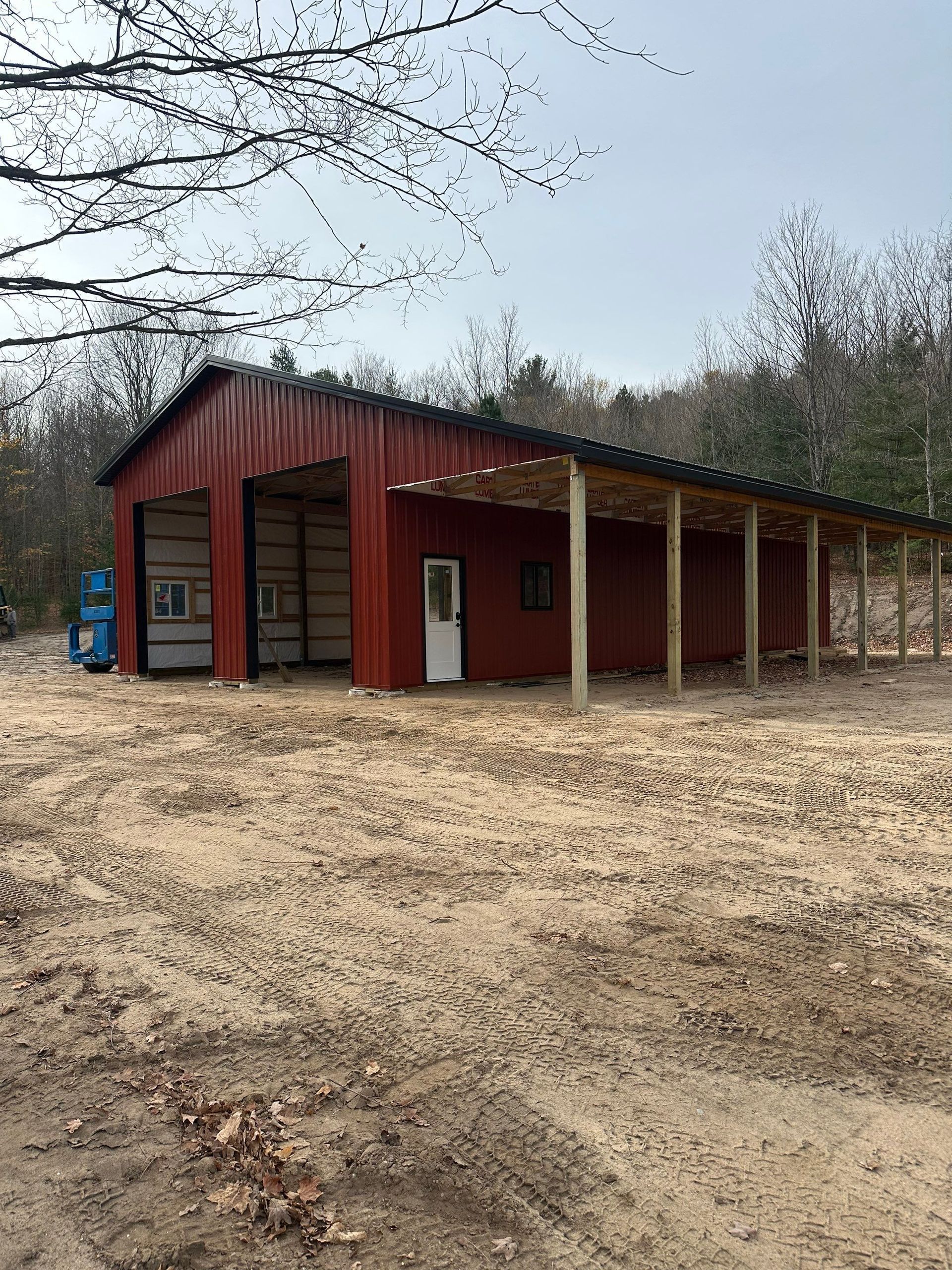 Red metal building with garage doors, covered porch, and white door, in a sandy clearing.