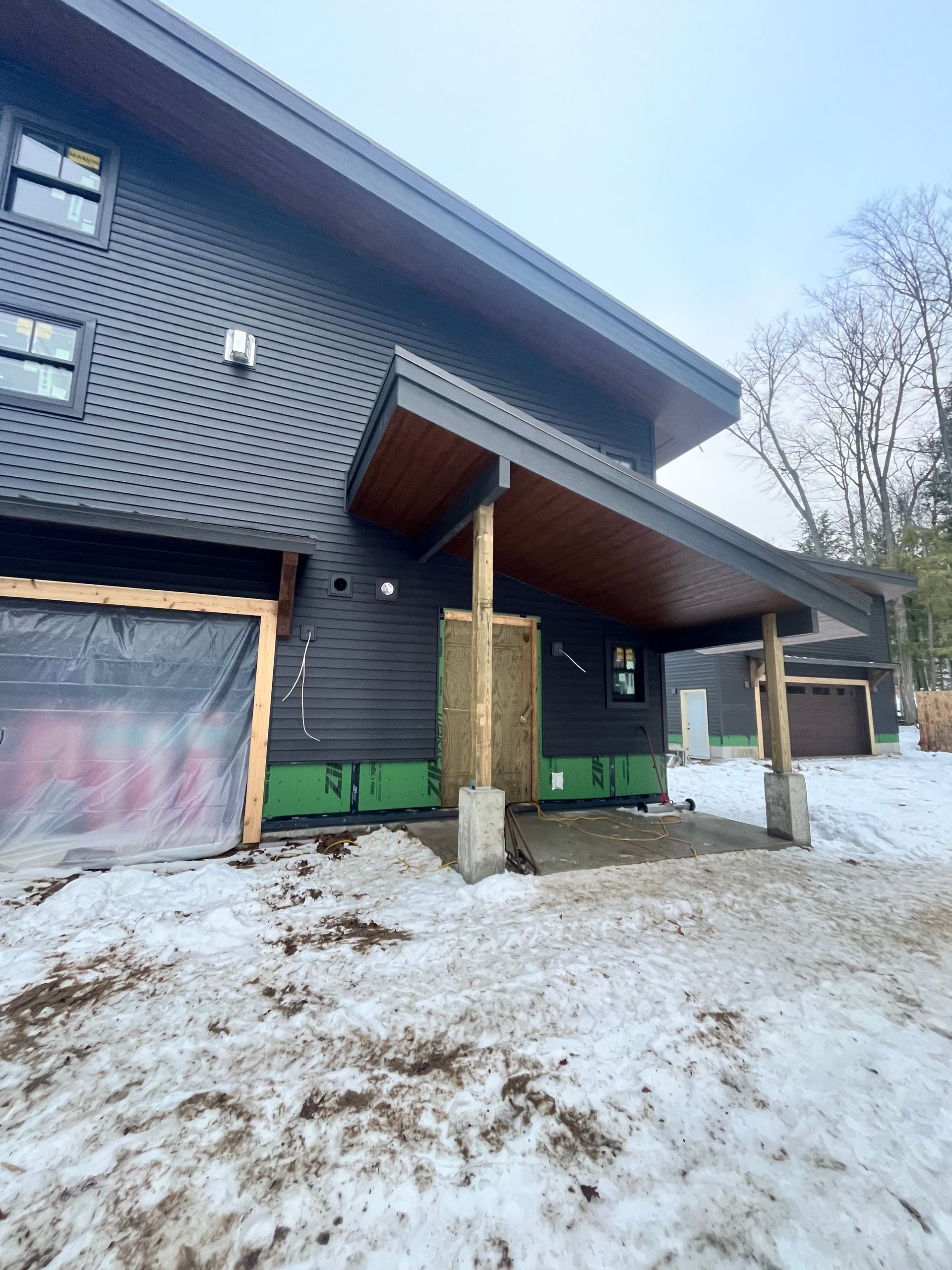 Black-sided modern house with a wooden overhang and snow-covered ground.