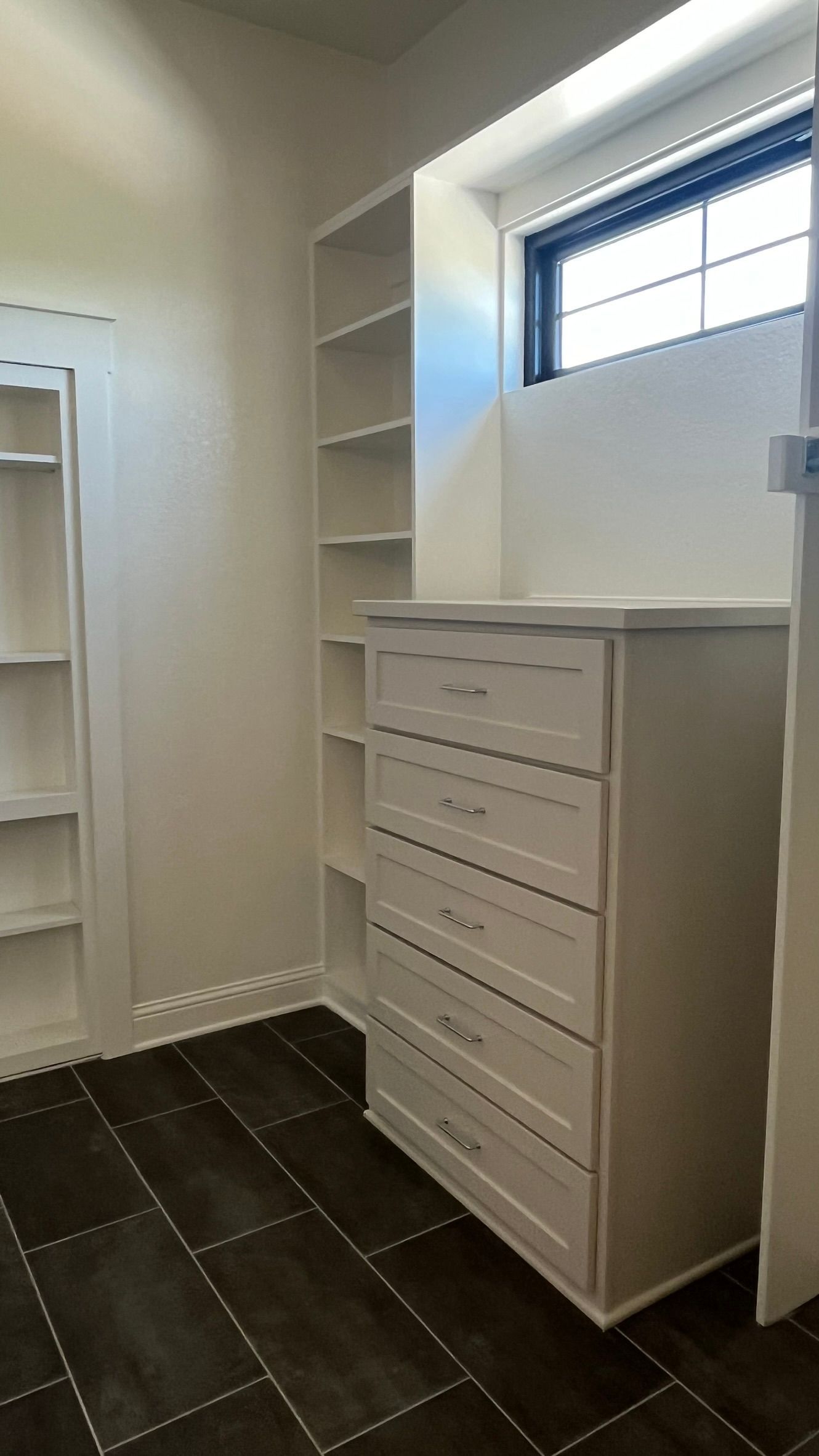 A walk in closet with a dresser , shelves , and a window
