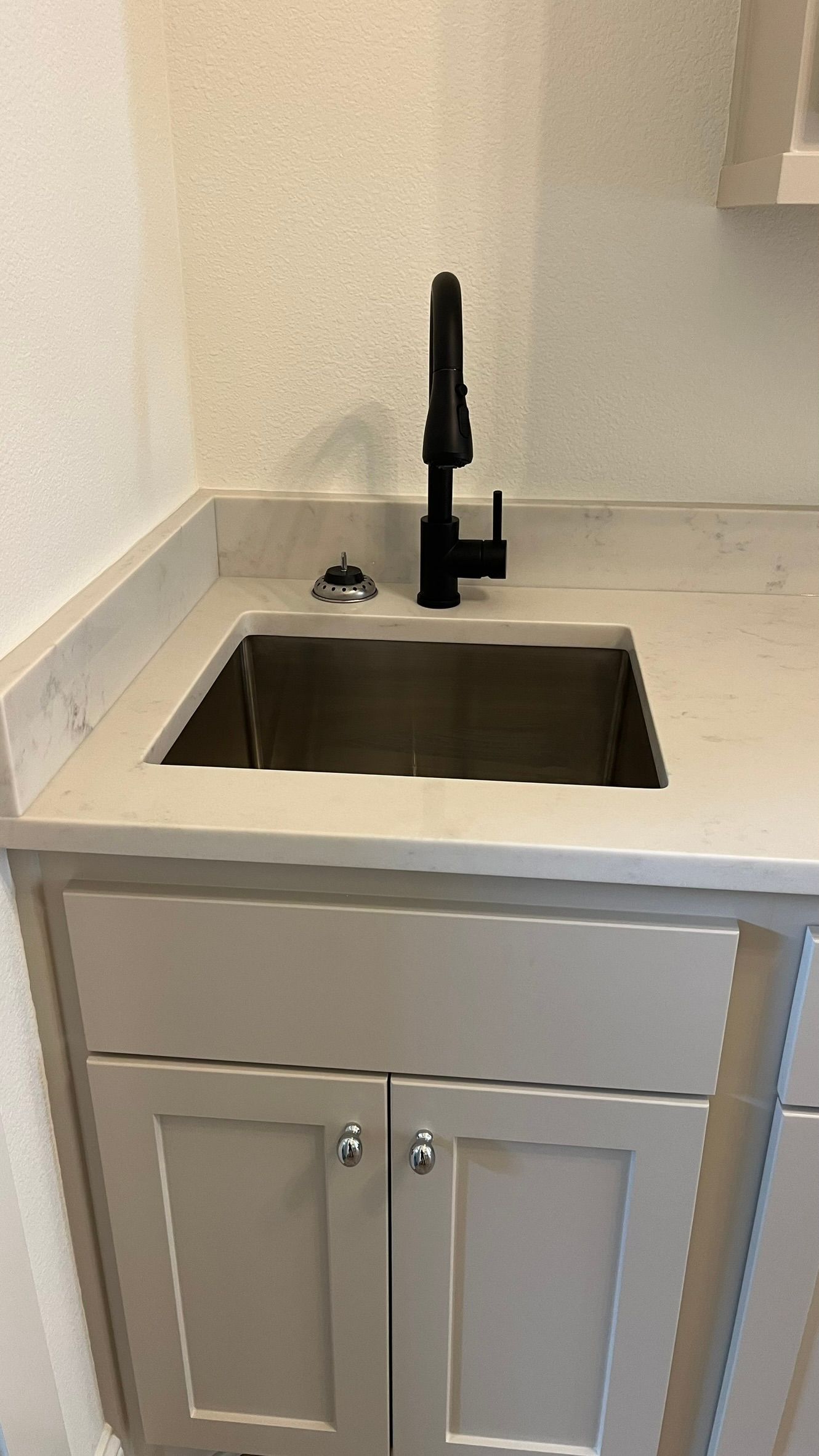 A kitchen sink with a black faucet and beige cabinets