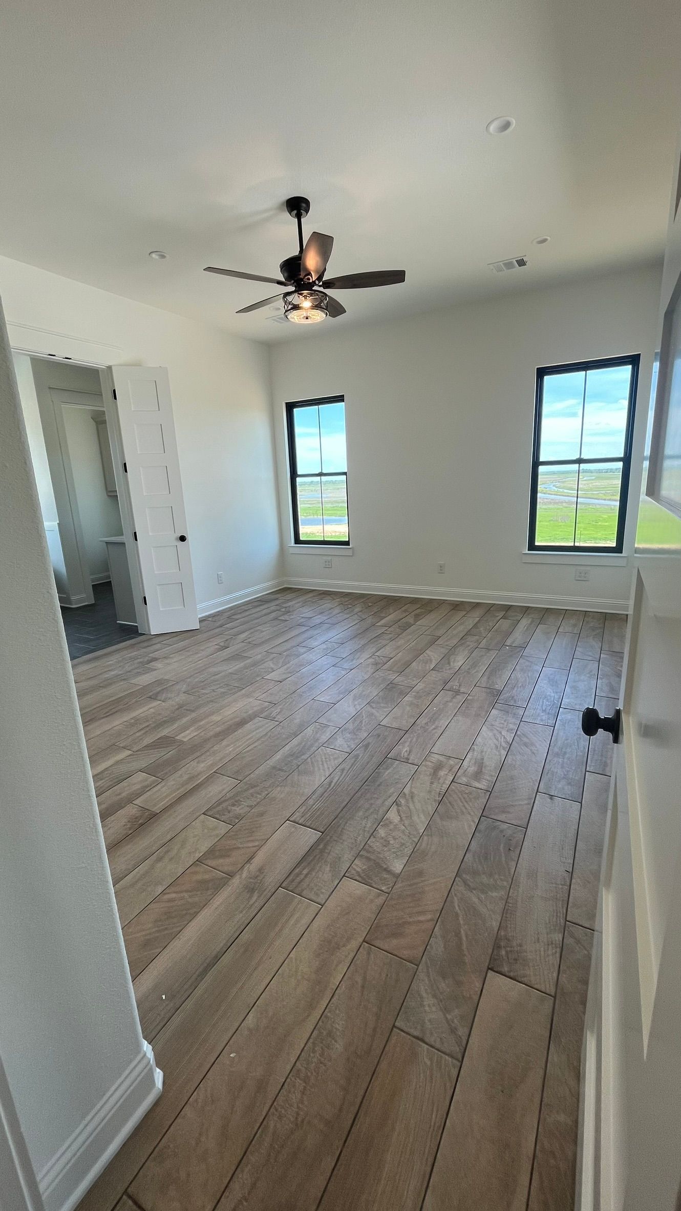 An empty master bedroom with hardwood floors and a ceiling fan