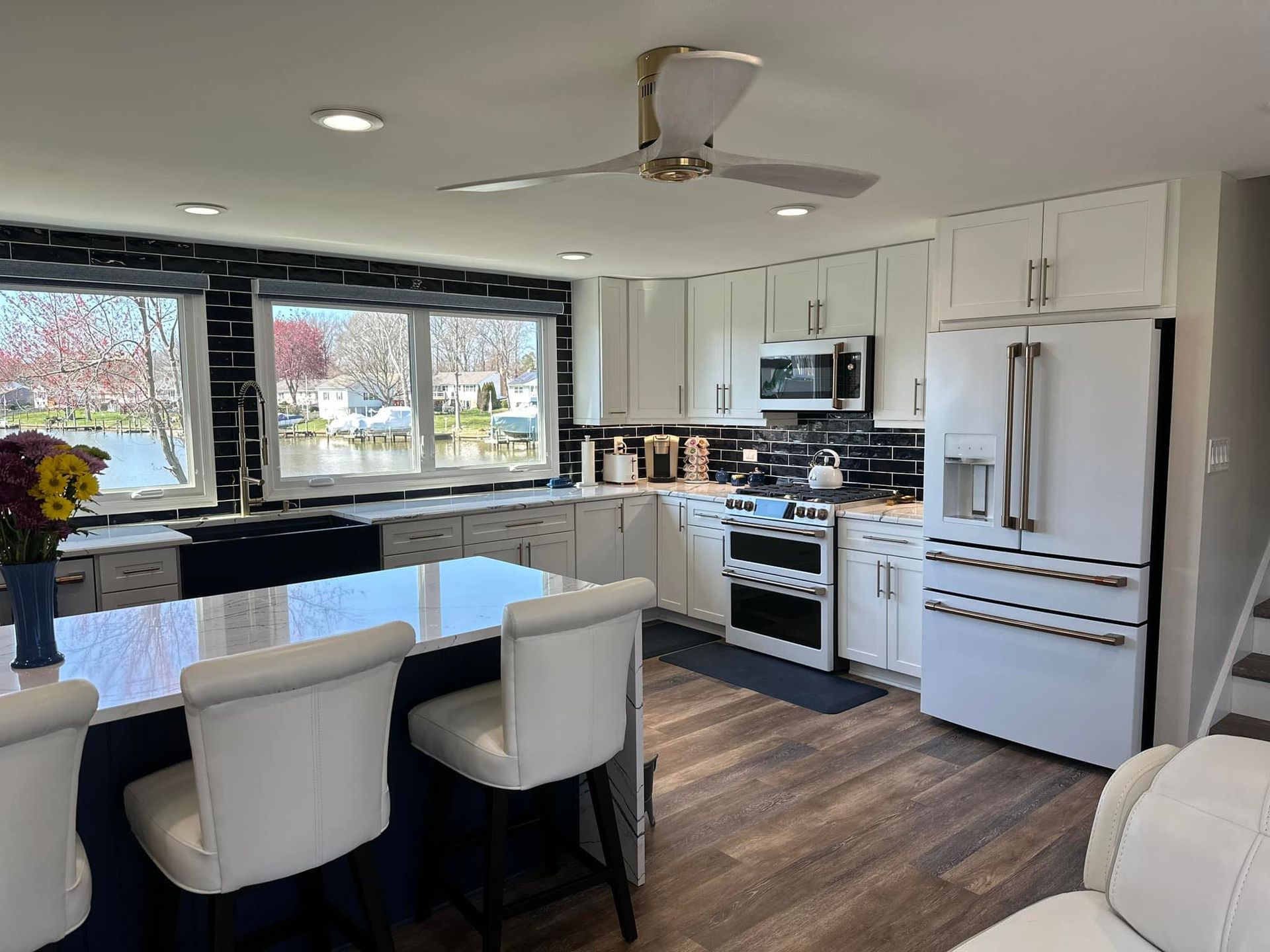 a kitchen with white cabinets , a refrigerator , a stove , and a ceiling fan .