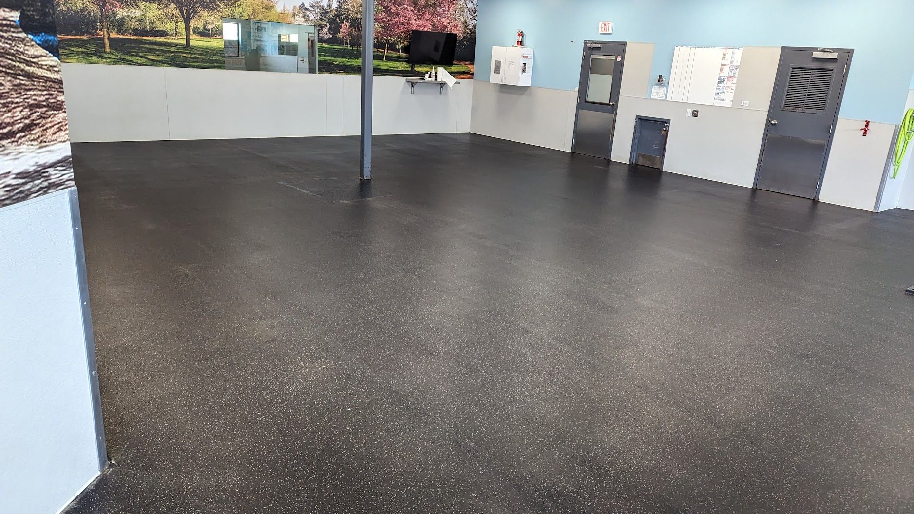 Empty indoor room with black speckled floor, white walls, and a central support pole